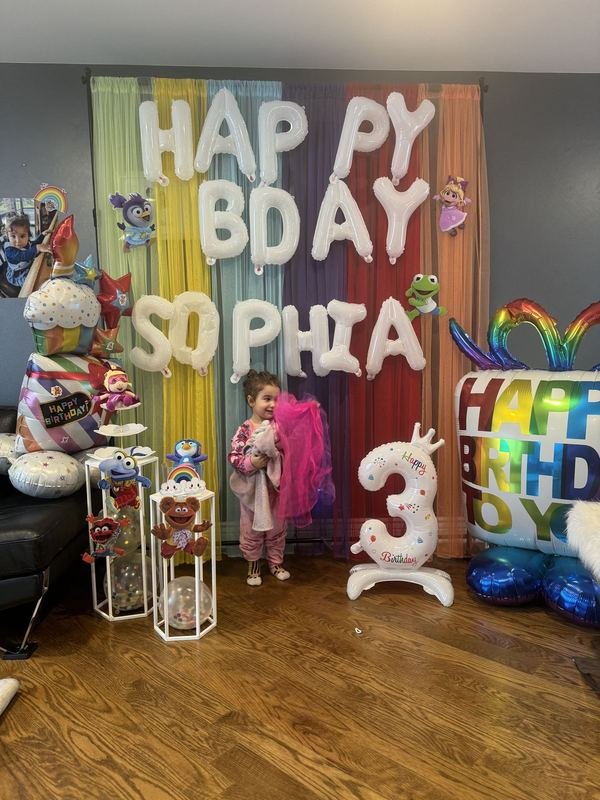 Rainbow streamer wall with white letter balloons and a number three